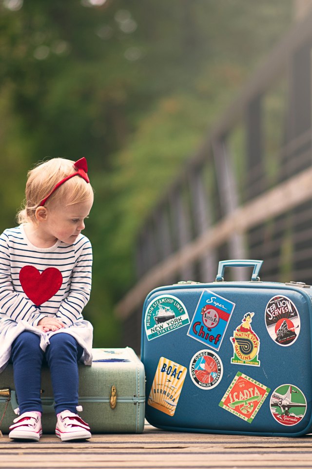 Маленькая девочка сидит на мосту с чемоданами