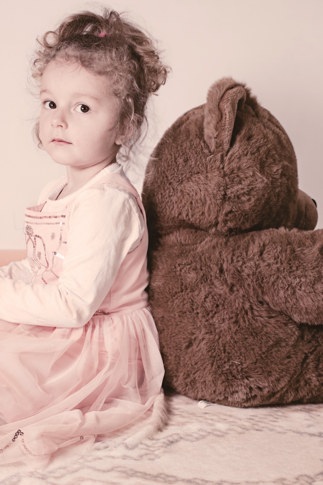 Маленькая девочка сидит с большим медведем