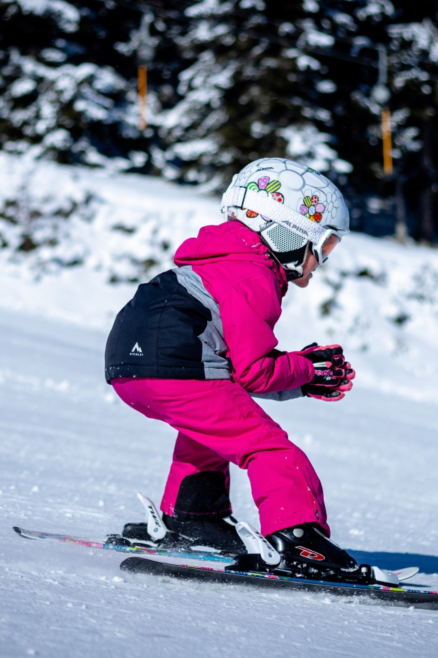 Маленькая девочка едет на лыжах по снегу