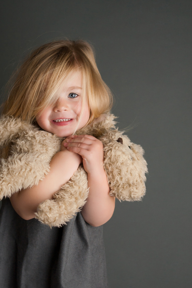 Маленькая девочка с игрушечным медвежонком в руках  на сером фоне 