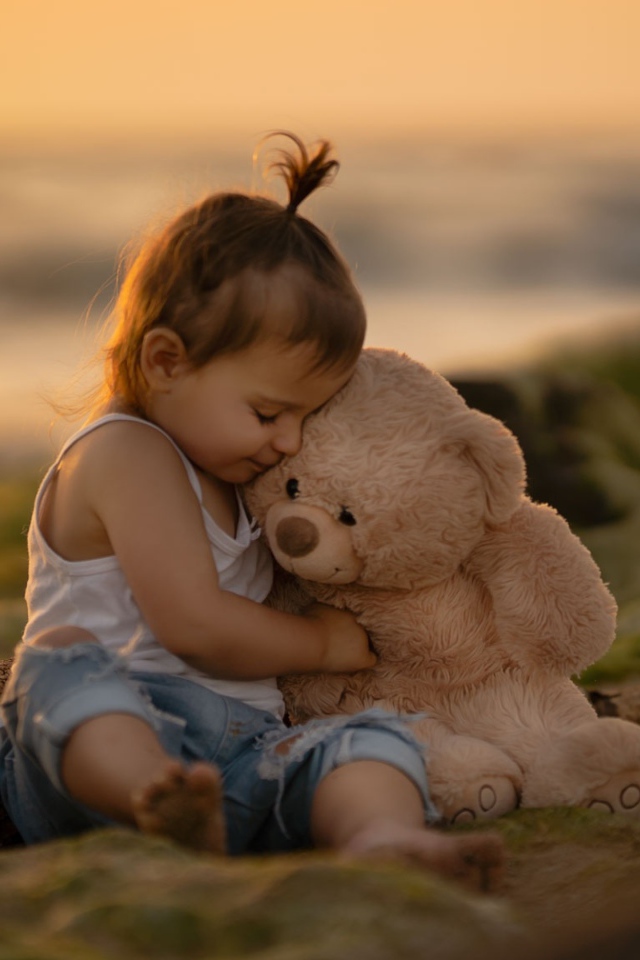 Маленькая девочка с игрушечным медведем сидит на камне