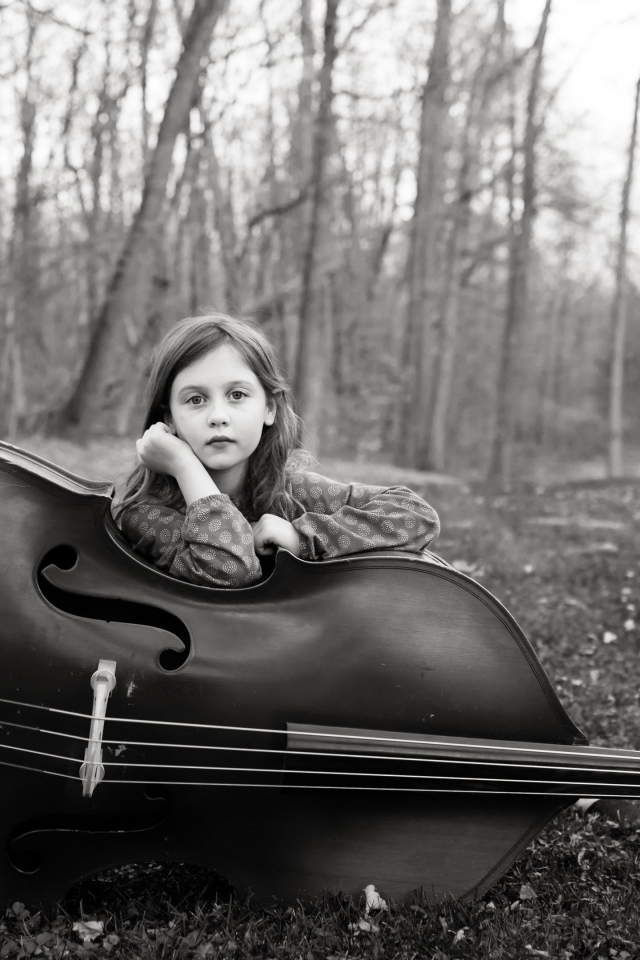 Маленькая девочка с виолончелью сидит в парке