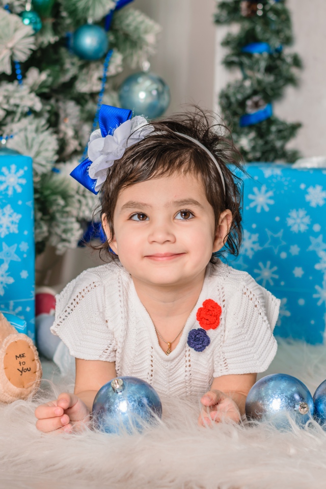 Маленькая девочка с подарками и игрушками под елкой 