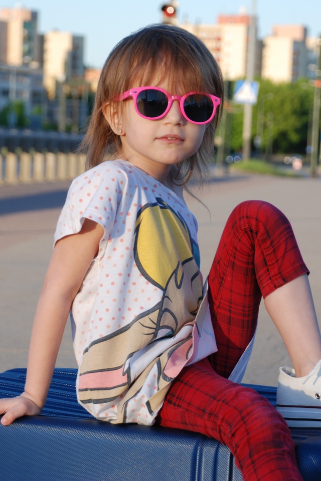 Маленькая девочка в очках сидит на чемодане