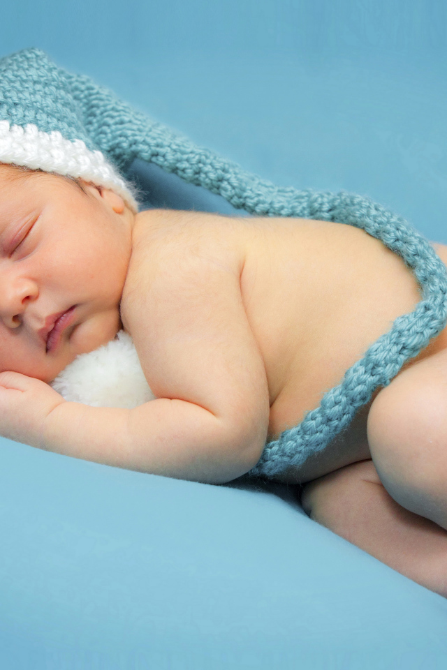 Маленький спящий ребенок в шапке на голубом фоне 