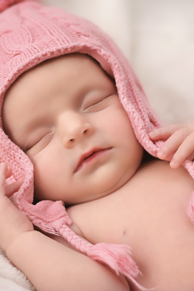 Маленький спящий ребенок в розовой вязаной шапке 