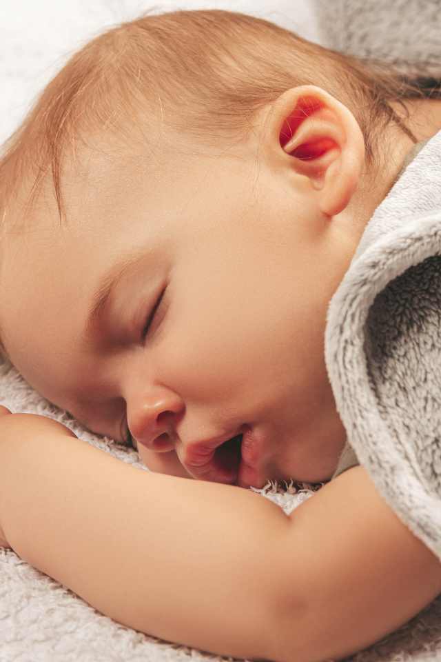 Маленький спящий ребенок под серым покрывалом 