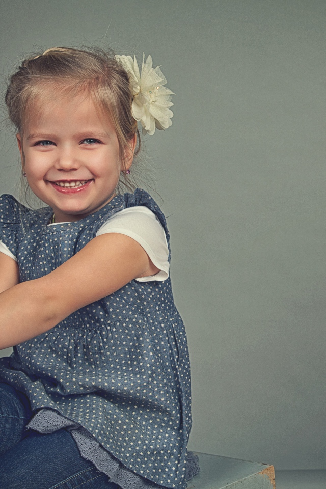 Маленькая улыбающаяся девочка с бантом на сером фоне 