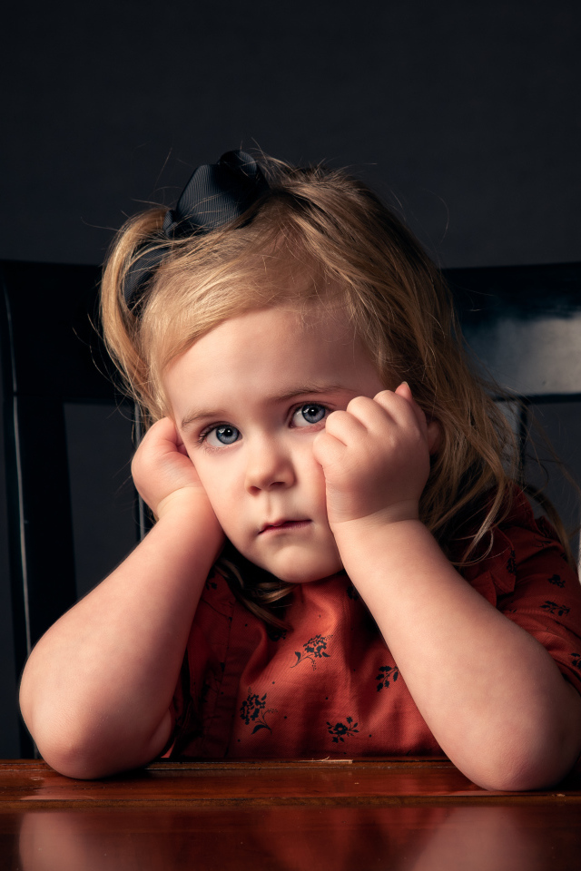 Грустная маленькая девочка сидит на черном стуле