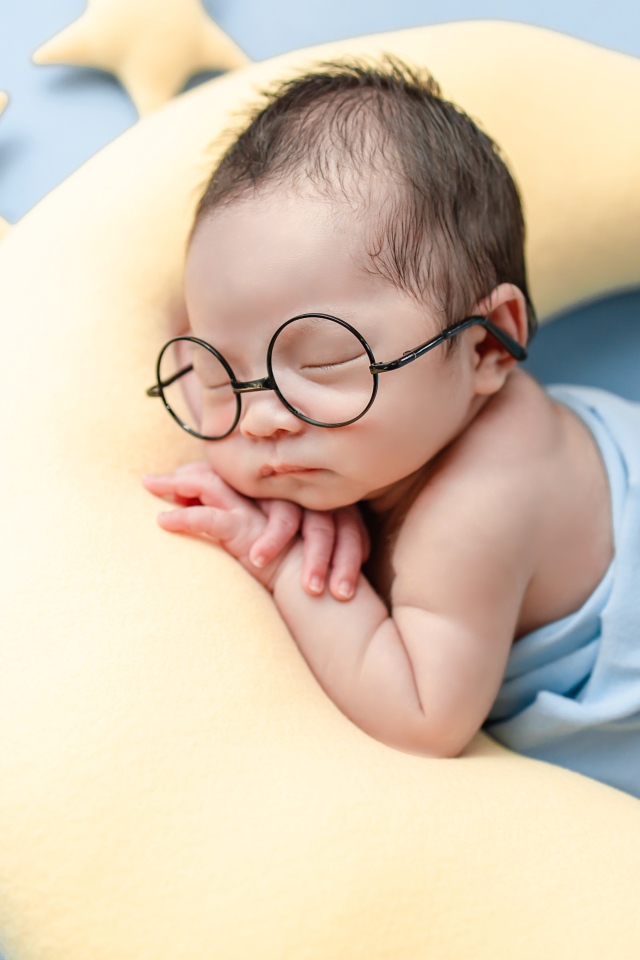 Спящий ребенок в очках на подушке в форме месяца