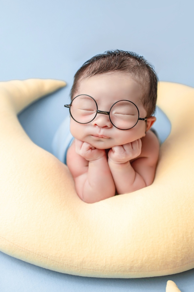 Спящий грудной ребенок в очках на желтой подушке 