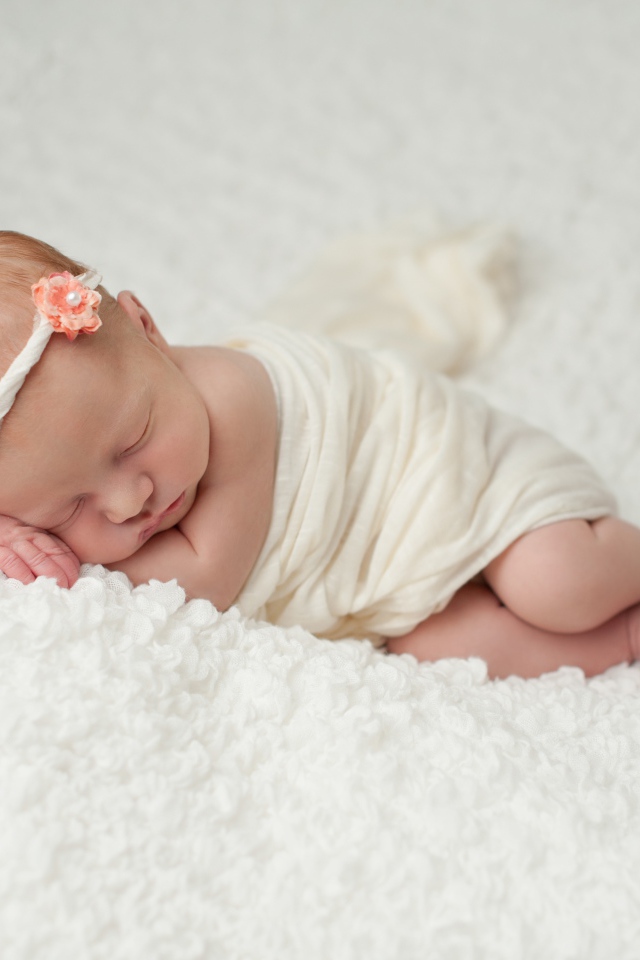 Маленький грудной ребенок спит на белом покрывале 