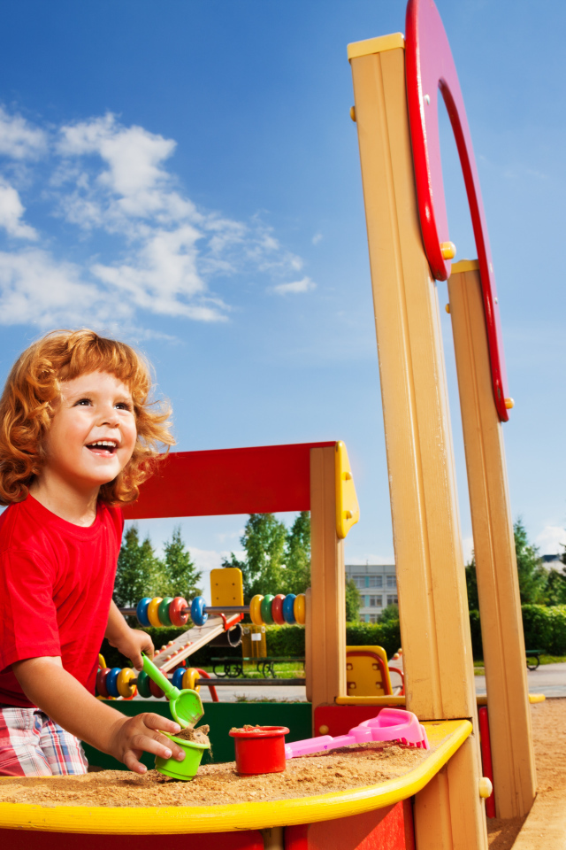 Улыбающийся мальчик в песочнице на детской площадке 