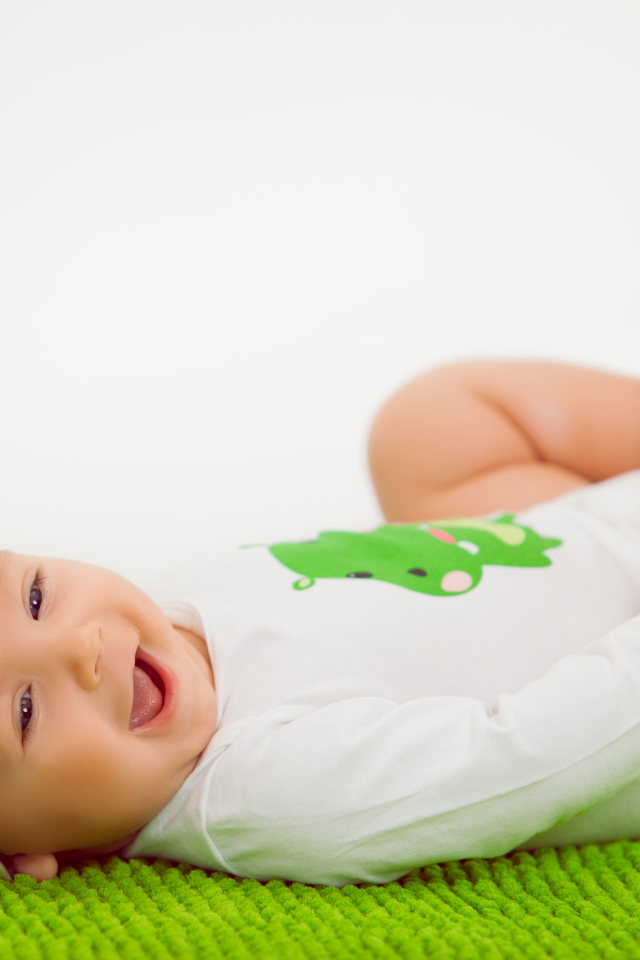 Улыбающийся маленький ребенок лежит на зеленом покрывале 