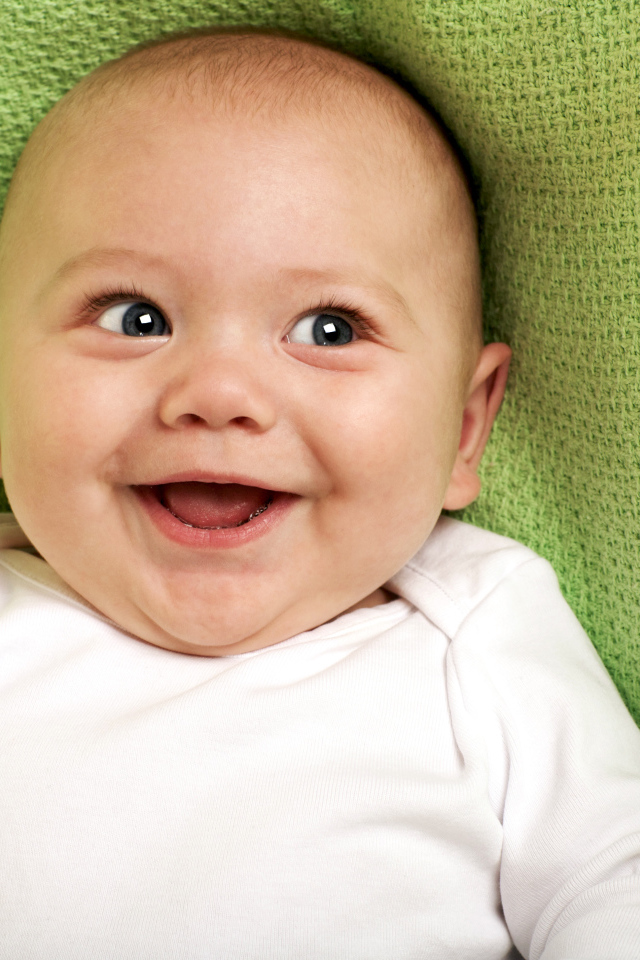 Улыбающийся маленький ребенок на зеленом покрывале 