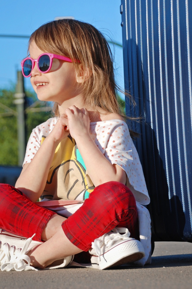 Улыбающаяся маленькая девочка в очках с чемоданом