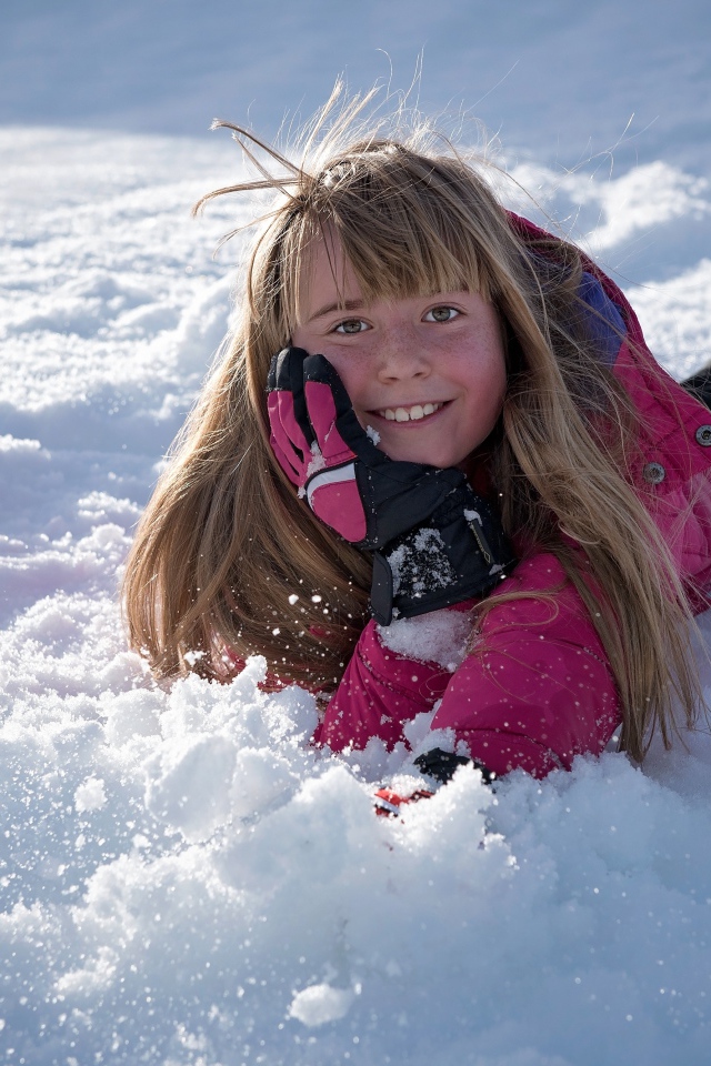 Улыбающаяся маленькая девочка лежит на снегу
