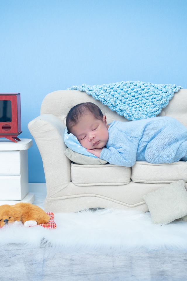 Ребенок спит на маленьком диване на фоне голубой стены