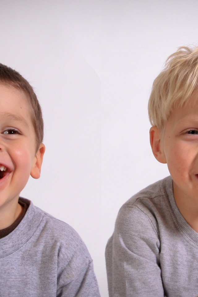 Два маленьких мальчика смеются на сером фоне