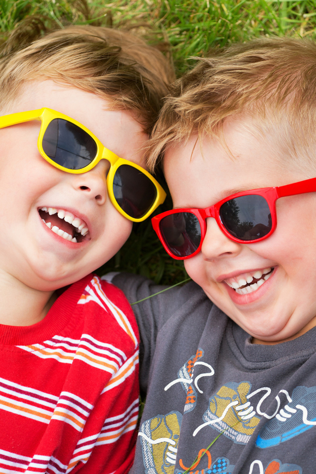 Два улыбающихся мальчика в очках на зеленой траве 