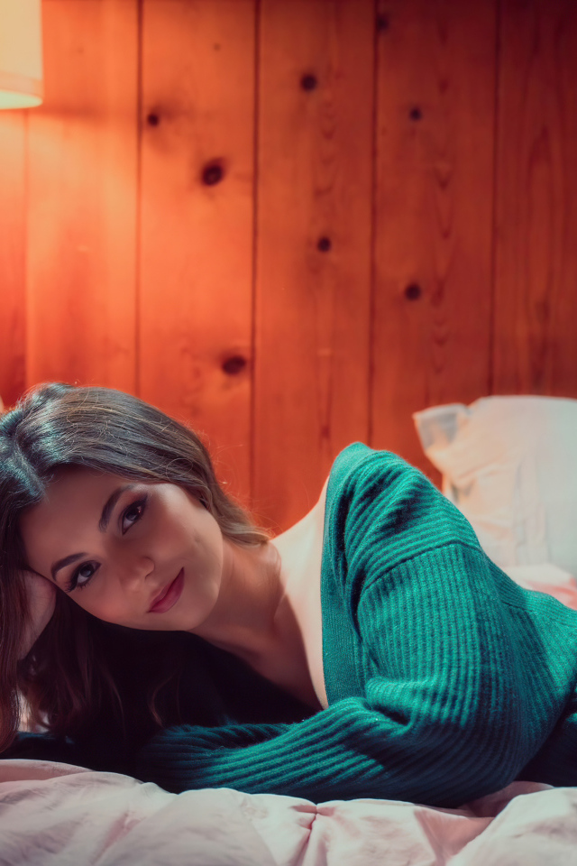 Актриса  Виктория Джастис в зеленом свитере на кровати