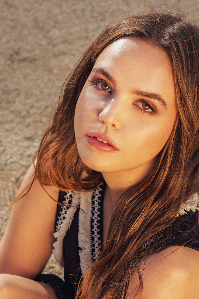 Кареглазая актриса Бэйли Мэдисон сидит на песке