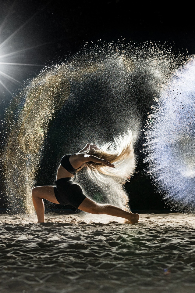 Девушка в черном костюме танцует на песке 