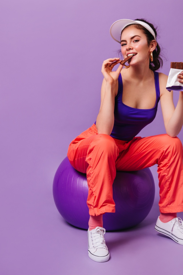 Девушка с шоколадкой сидит на фитболе