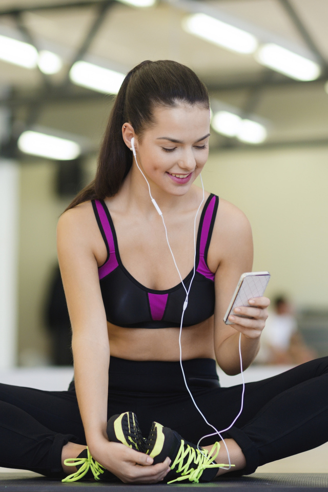 Спортивная девушка сидит на коврике с телефоном 