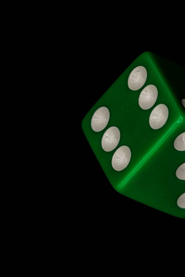 Зеленый игральный кубик на черном фоне