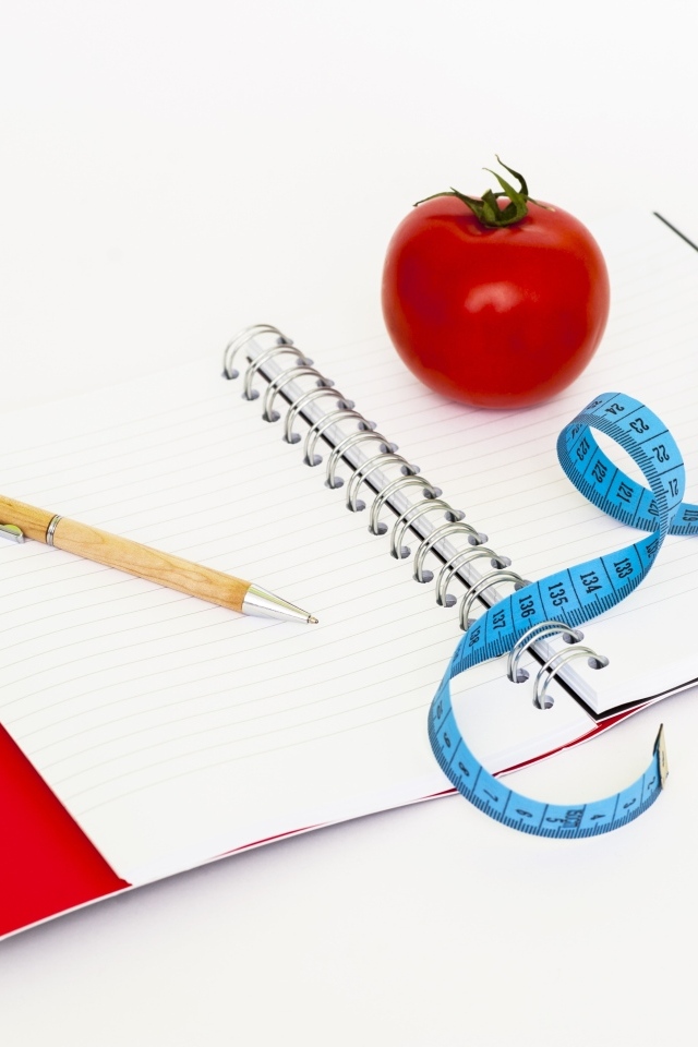 Блокнот с ручкой на столе с сантиметром и помидором