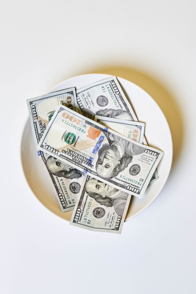 Доллары на тарелке на сером фоне со столовыми приборами