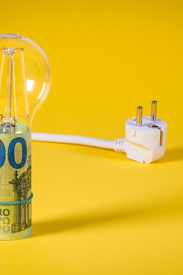 Лампочка с деньгами и розеткой на желтом фоне