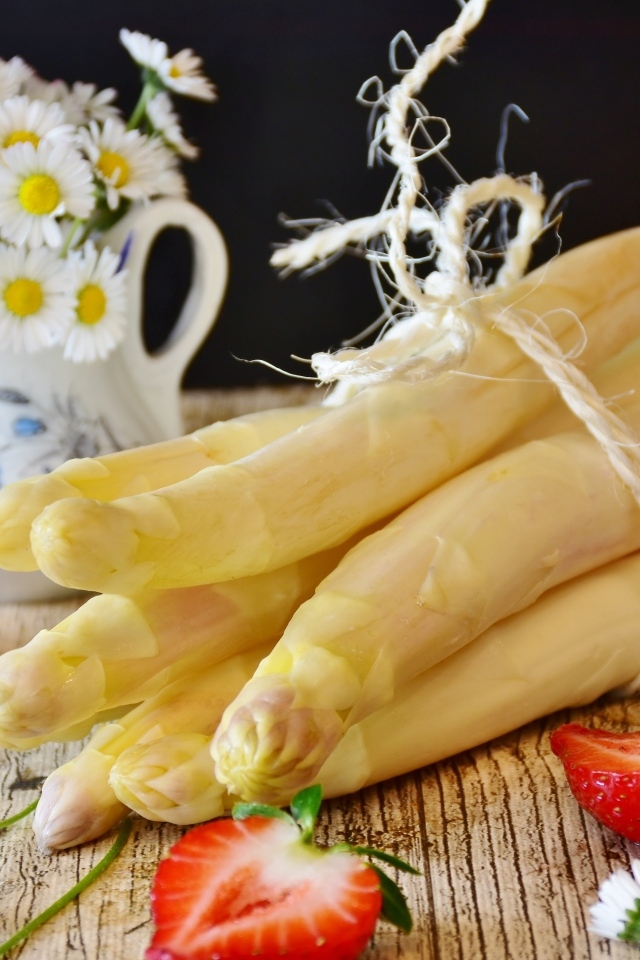 Спаржа на столе с ромашками и ягодами клубники