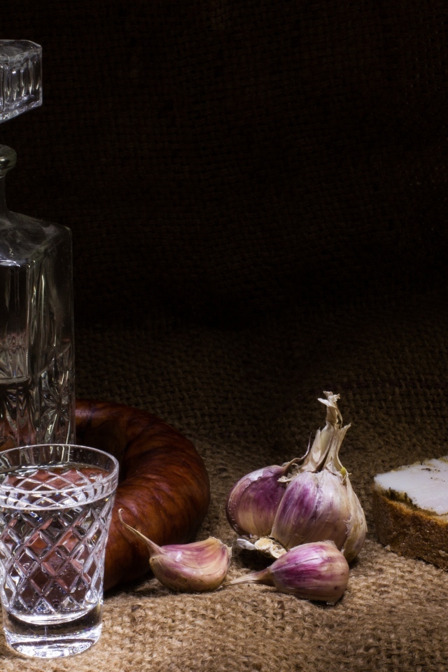 Бутылка водки на столе с салом, колбасой и чесноком