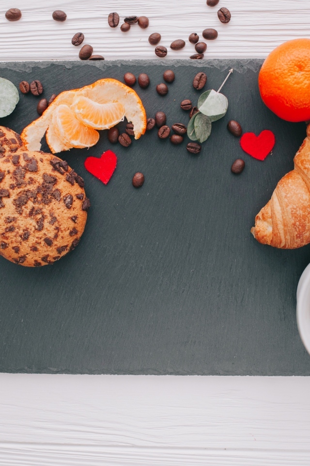 Круассан на столе с печенье, чашкой кофе и мандарином