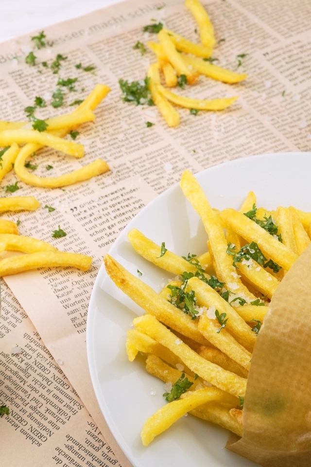 Картофель фри на столе с газетой, солью и зеленью 