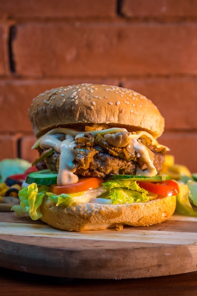 Большой аппетитный гамбургер на фоне стены