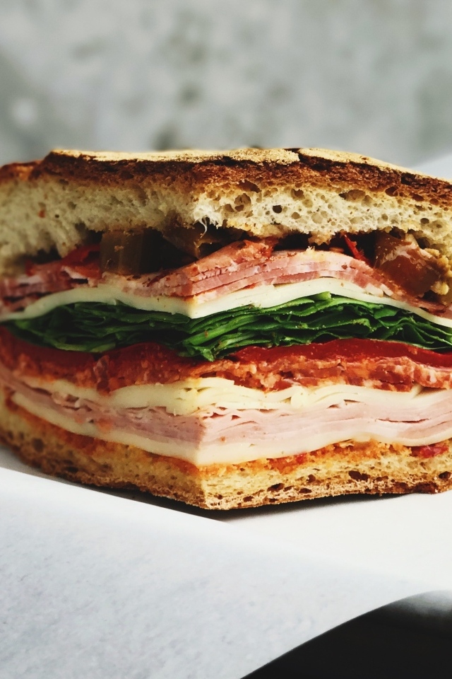 Кусок булки с колбасой, ветчиной и листьями салата