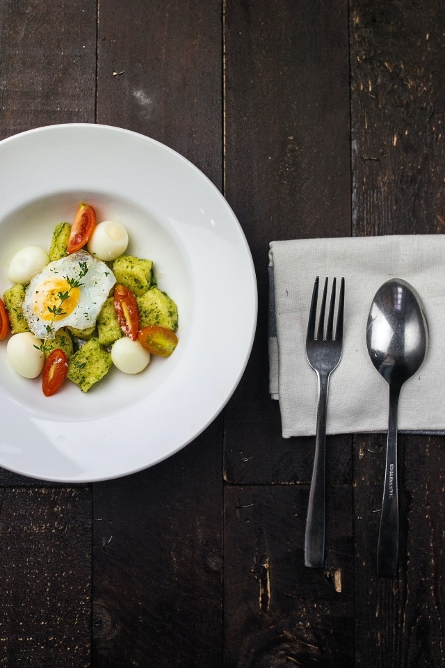 Яичница с овощами в белой тарелке на столе со столовыми приборами