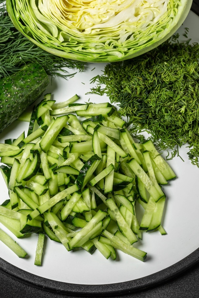 Нарезанные огурцы на столе с капустой и укропом