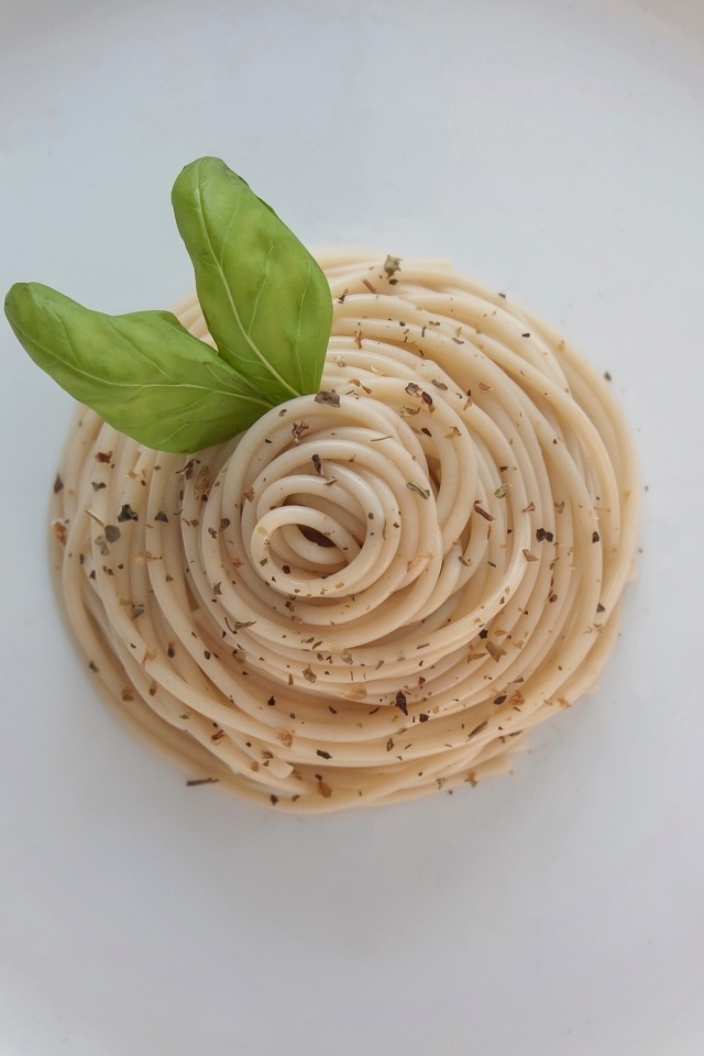 Спагетти с листьями базилика на белой тарелке