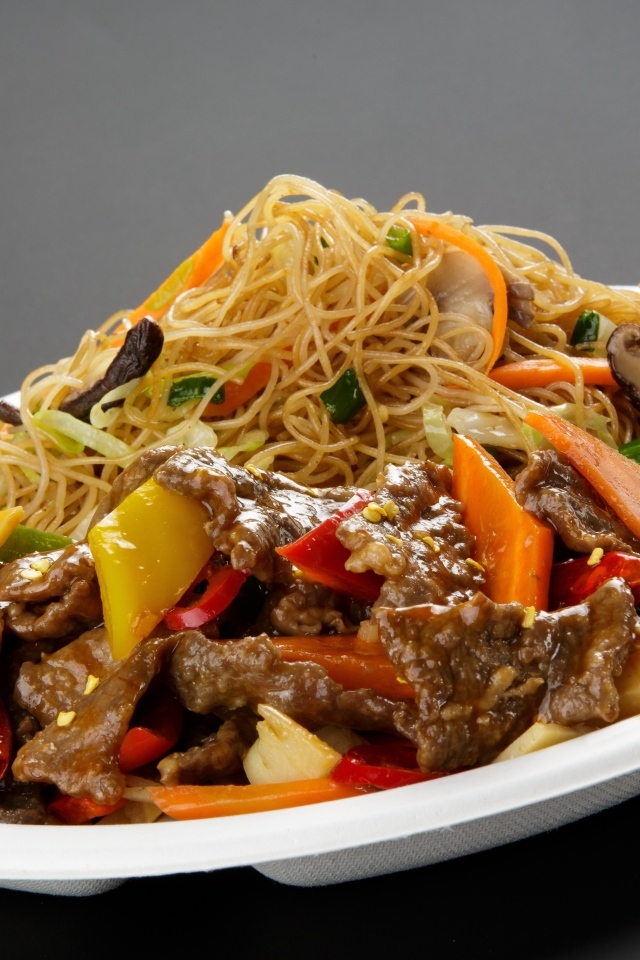 Острая лапша с грибами на белой тарелке на сером фоне