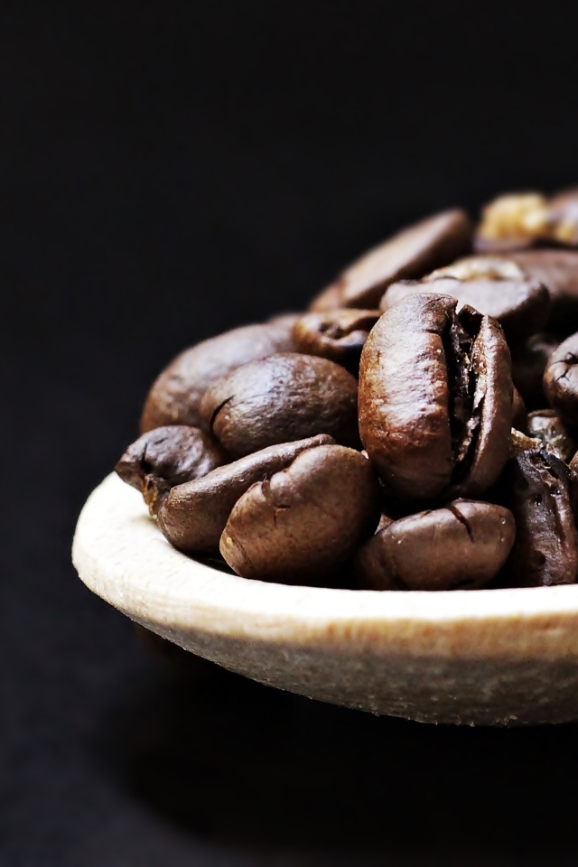 Зерна кофе на деревянной ложке на черном фоне