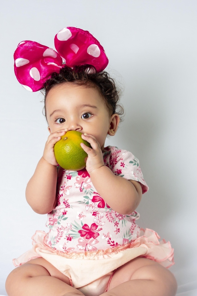 Девочка с большим бантом на голове ест апельсин