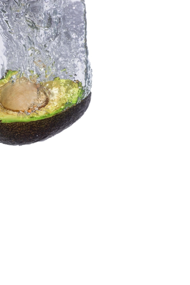 Половина авокадо падает в воду на белом фоне