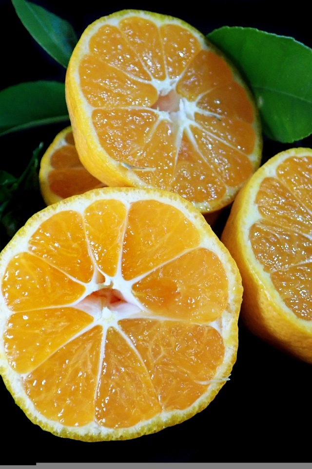 Половинки мандарина с зелеными листьями на черном фоне