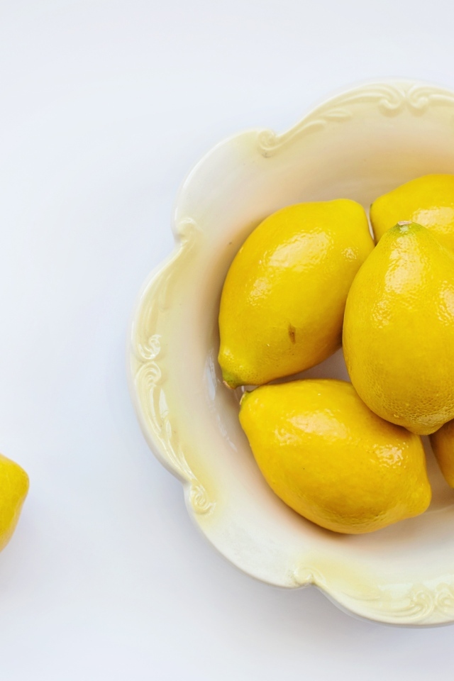 Крупные желтые лимоны в тарелке на белом фоне