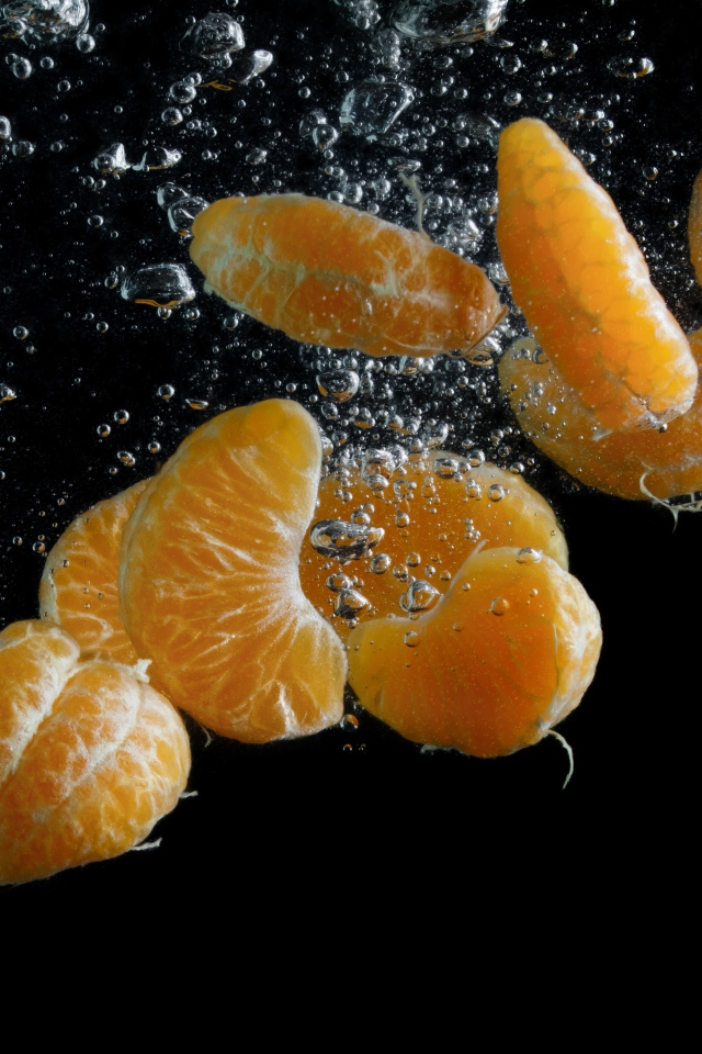 Дольки мандарина в воде на черном фоне