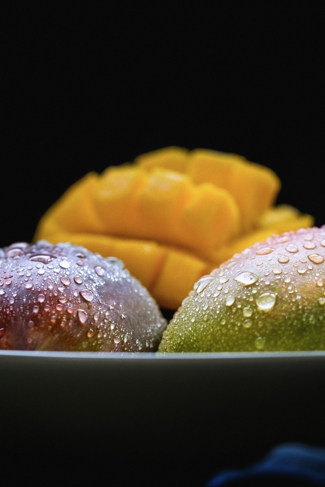 Плоды манго на тарелке на черном фоне